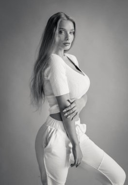 Beyaz takım elbiseli güzel bir sarışının stüdyoda poz verirken siyah-beyaz fotoğrafı.