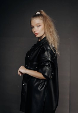 Güzel bir kız, sarı saçlı şık bir bluz, şort ve deri gömlekli koyu bir arka planda poz veriyor..