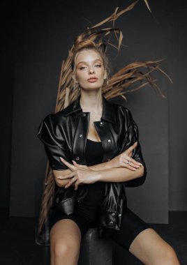 Şık bir saç stili olan şık bir kız kuru sazlıkların yanında gri bir arka planda oturuyor..