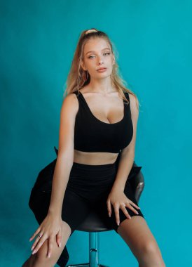 Stüdyoda bir bar taburesinde oturan muhteşem sarışın. Turkuaz arkaplan.