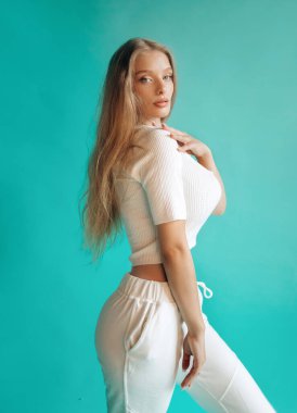 Stüdyoda turkuaz arka planda poz veren beyaz spor elbiseli lüks sarışın..