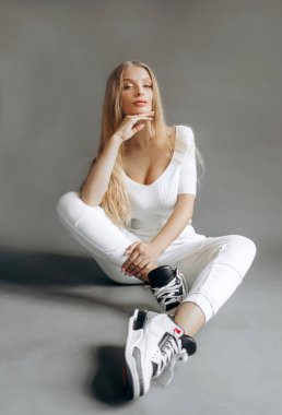 Beyaz takım elbiseli güzel bir kız stüdyoda gri bir arka planda oturuyor..