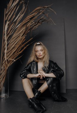 Gri bir arka planda oturan siyah şık takım elbiseli güzel sarışın bir manken..