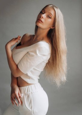 Beyaz spor kıyafetli güzel sarışın gri arka planda stüdyoda poz veriyor..