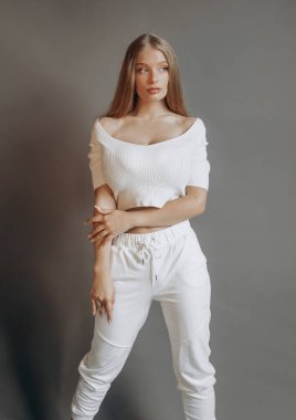 Beyaz spor kıyafetli güzel sarışın gri arka planda stüdyoda poz veriyor..