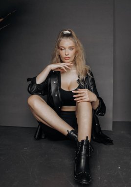 Gri bir arka planda oturan siyah şık takım elbiseli şık sarışın manken..