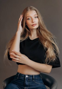 Siyah bluzlu, sandalyede oturan güzel sarışın kadının stüdyo portresini kapat. Mavi gözler, genç ve narin.