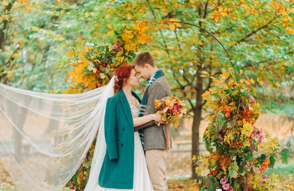 新婚夫婦が結婚式の日にアーチの近くに立っている 秋の公園 — ストック写真
