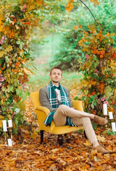 Şık takım elbiseli ciddi bir damat kemerin altında rahat bir sandalyede oturuyor..