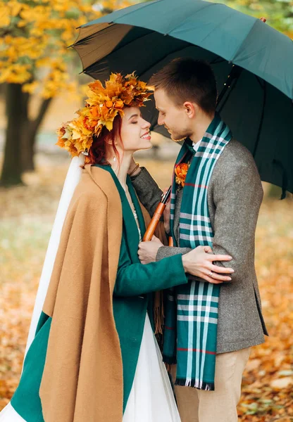 Şık sonbahar kıyafetleri içinde şemsiyenin altında öpüşen güzel yeni evliler..