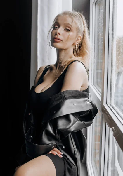 Göz kamaştırıcı, siyah elbiseli, pencerenin yanında poz veren sarışın..