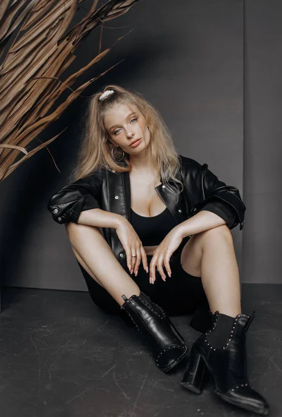 Gri bir arka planda oturan siyah şık takım elbiseli şık sarışın manken..