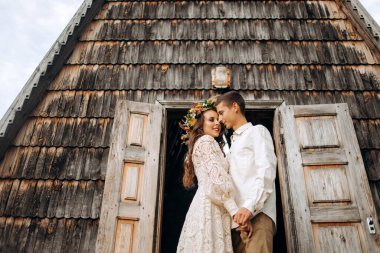 Aşık düğün çifti, parkın ortasında, perili ahşap bir evin önünde öpüşüyor.