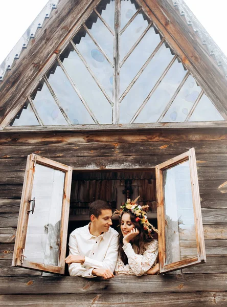 木造の家の窓に抱擁に立ってお祝いの衣装でかわいいカップル — ストック写真