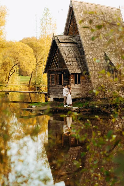 湖の近くの秋の公園で木製の気まぐれな居心地の良い家と愛のカップル — ストック写真