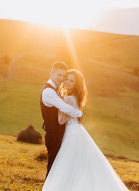 Yeni evliler gün batımında bir dağın tepesinde sarılıyorlar..