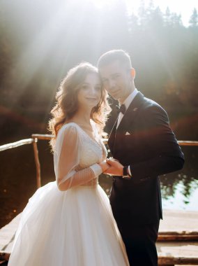 Birbirini seven genç bir çift birbirlerinin gözlerinin içine bakıyor, bir dağ gölünün yakınındaki rıhtımda el ele duruyorlar.