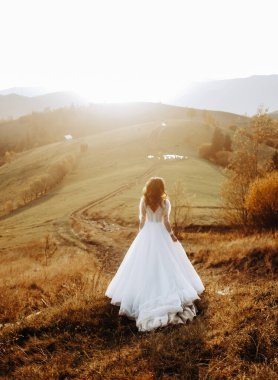 Güzel gelin bir dağ çayırında yürüyor