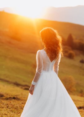 Tepe çayırında duran harika gelin sonbahar günbatımının tadını çıkarıyor. Bir dağ tepesi. İnanılmaz manzara..