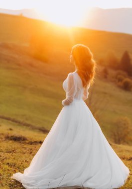 Şatafatlı gelin bir tepedeki çayırda duruyor ve sonbahar günbatımının tadını çıkarıyor. Bir dağ tepesi. İnanılmaz manzara..