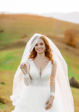 Duvağı olan güzel gelin, dağ manzarasının arka planında duruyor..