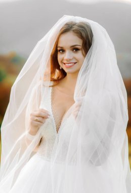 Duvağı olan sevimli gelin, dağ manzarasının arka planında duruyor..