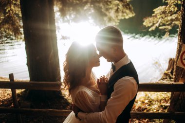 Turkuaz bir gölün arka planında genç bir çiftin portresi. Güneş ışınları çiftin yüzünü okşar..