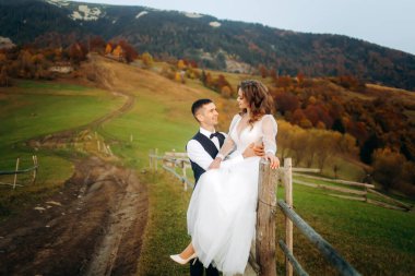 Yeni evliler, sonbahar dağlarında tahta bir çitin yanında durur..