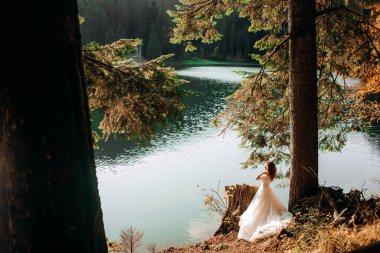 Zarif gelin bir dağ gölündeki ağacın yanında poz verir..