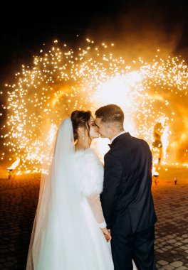 Yeni evliler akşam havai fişeklerin arka planında öpüşürler.