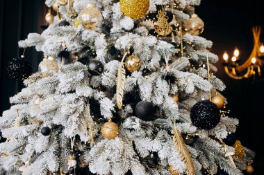 Güzel bir Noel ağacı, siyah ve altın renkli Noel ağacı oyuncaklarıyla süslenmiş geniş bir odada duruyor..