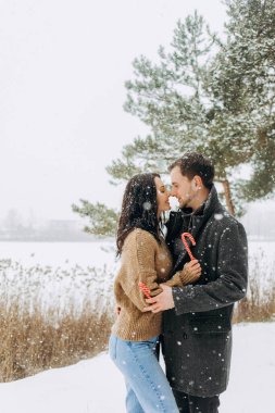 Karlı bir parkta ellerinde lolipoplarla poz veren sevimli bir çift..