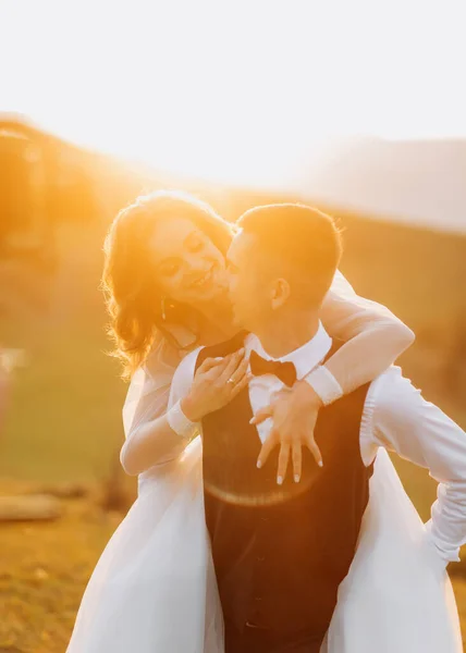 Precioso Novio Lleva Novia Sobre Sus Hombros Las Colinas Atardecer —  Fotos de Stock