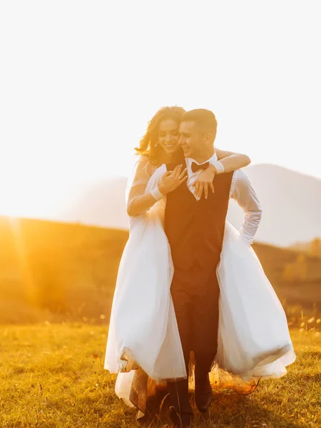 Glad Brudgum Bär Sin Brud Sina Axlar Kullarna Vid Solnedgången — Stockfoto