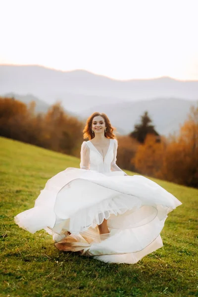 Gelinlik giymiş çılgın gelin gün batımında dağlarda koşuyor.