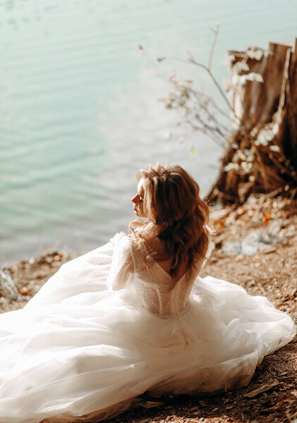 The young bride sitting near the lake in the sun, caressing her face.