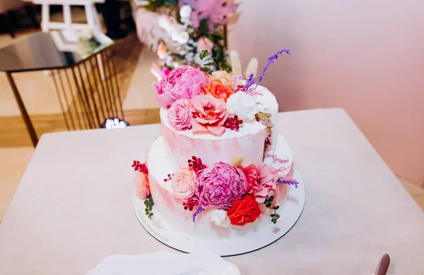 Beyaz düğün pastası pembe ve beyaz şakayık çiçekleri ve güllerle.