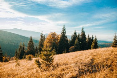 Yükselen güneşin ve bulutlu gökyüzünün altındaki yüksek dağların güzel bir yatay görüntüsü.