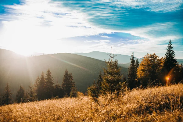 Yükselen güneşin ve bulutlu gökyüzünün altındaki yüksek dağların güzel bir yatay görüntüsü.