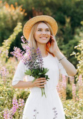 Beyaz elbiseli, kısa saçlı genç bir sarışın. Kadın lup tarlasında poz veriyor.
