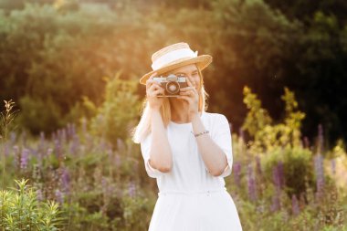 Lupin tarlasında poz veren elinde kamera olan güzel sarışın kadın..