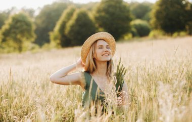 Hasır şapkalı, yeşil takım elbiseli, buğday tarlasında elinde çivilerle poz veren güzel bir sarışın.