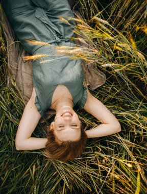 Yeşil takım elbiseli lüks sarışın gün batımında bir tarlada buğday başakları arasında yatıyor.