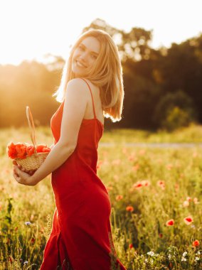 Haşhaş tarlasında poz veren kırmızı elbiseli güzel sarışın kadın elinde haşhaş dolu bir sepet tutuyor..