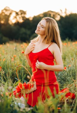Kırmızı elbiseli inanılmaz güzel bir kadın elinde bir buket gelincikle bir çiçek tarlasında oturuyor..
