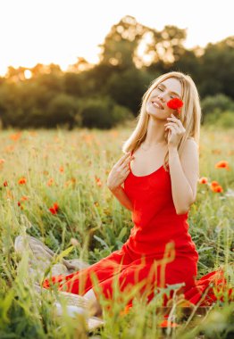 Kırmızı elbiseli enfes sarışın haşhaş tarlasında poz veriyor.