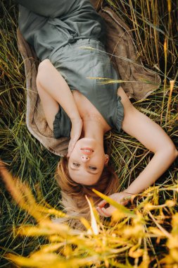 Yeşil takım elbiseli lüks sarışın gün batımında bir tarlada buğday başakları arasında yatıyor.