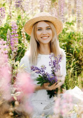 Beyaz elbiseli, kısa saçlı genç bir sarışın. Kadın lup tarlasında poz veriyor.