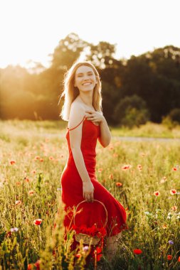 Haşhaş tarlasında poz veren kırmızı elbiseli tatlı sarışın kadın elinde haşhaş dolu bir sepet tutuyor.