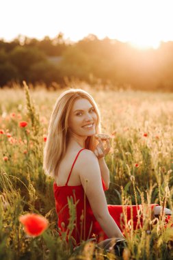 Kırmızı elbiseli güzel sarışın gün batımında çikolata parçacıklı kurabiye yiyor, gelincik tarlasında piknik yapıyor.